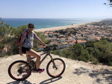 Photo d'une jeune fille sur son vélo avec en 2ème plan la plage et Leucate Plage vu d'en haut de la falaise